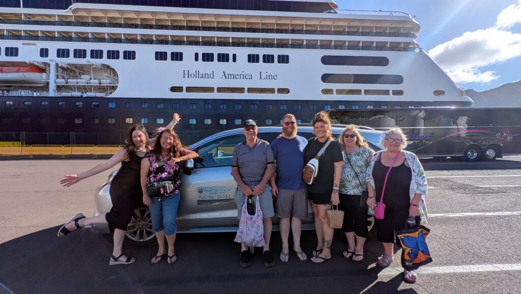 A group of people posing in front of a car, with a Holland America Line cruise ship in the background, captures the essence of a perfect getaway. The sunny weather adds to the idyllic atmosphere, making it feel like an adventure on par with exploring Kauai's stunning landscapes.